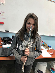 A young girl in a gray sweatshirt holding her Ted Brown Music Outreach flute.